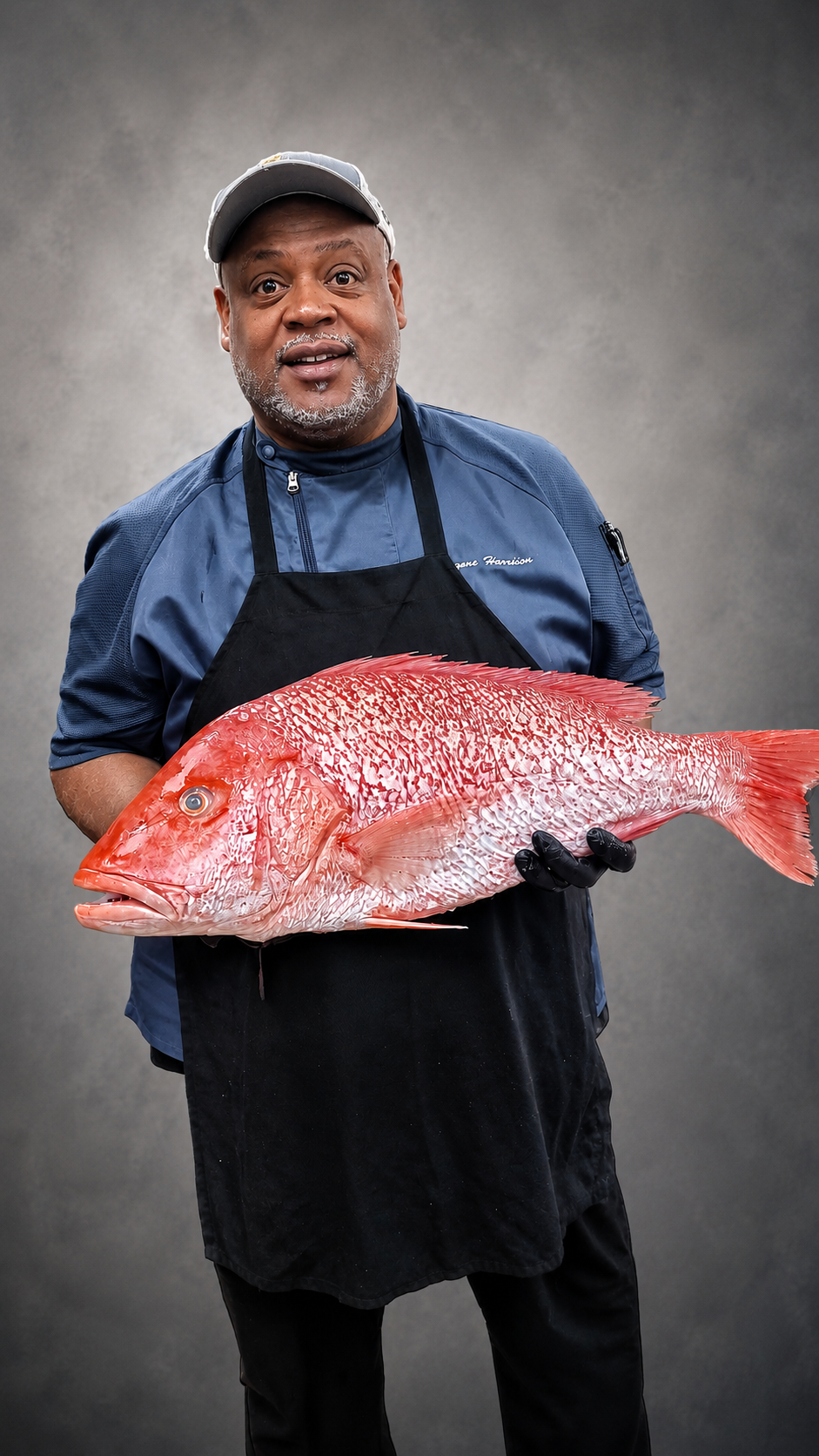 Chef Harrison holding a whole red snapper in a professional kitchen
